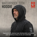 Man wearing black waterproof tech hoodie in rain, hood up, water beading on fabric